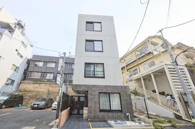 a tall white building on a street with buildings at 12 \u3068\u308a\u3063\u3071\u30fc\u305a\u30db\u30c6\u30eb\u9ad8\u7530\u99ac\u5834 in Tokyo