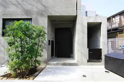 a concrete building with a black door and a tree at \u62b9\u8336\u5eb5\u4e09\u8336\u6771\u4eac Matcha-An Sancha Tokyo #202 in Tokyo