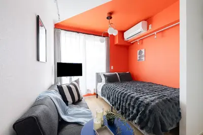 a bedroom with orange walls and a bed and a couch at ARiA STAY SHINAGAWA in Tokyo