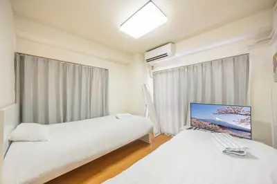 a bedroom with two beds and a monitor on the wall at Ikebukuro 8 min walk, Kanamecho 6 min walk, 25sqm room, 2 guests, Direct access to Shinjuku, Shibuya, Tokyo, Ueno, 2 single beds in Tokyo
