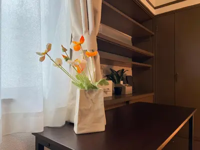 a vase with flowers on a table next to a window at nestay suite tokyo Takadanobaba in Tokyo