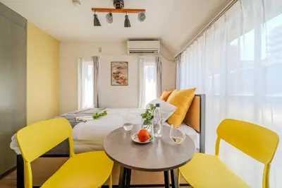 a room with a bed and a table with yellow chairs at T-Flat SASAZUKA in Tokyo