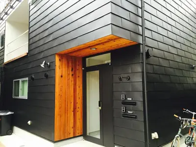a house with a black wall and a wooden door at Shimokitazawa Sanctuary , Spacious Stay for Families & Romantic Getaways in Tokyo