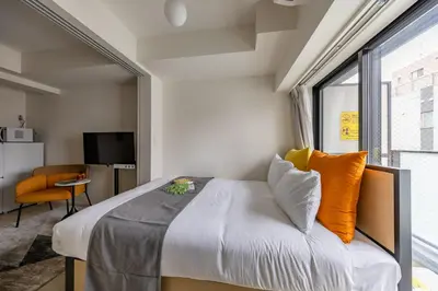 a bedroom with a bed with orange pillows and a window at Daffitto\u62bc\u4e0aI in Tokyo