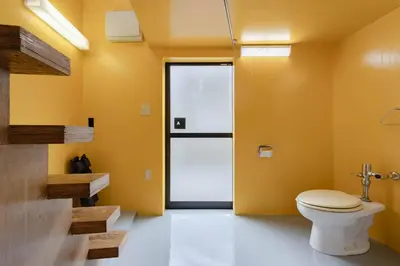 a bathroom with a toilet and a yellow wall at House Hotel Nakano TNA in Tokyo
