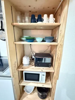a shelf with a microwave and dishes on it at Wabi Sabi Hostel Shinjuku West in Tokyo