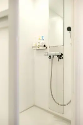 a shower in a white bathroom with a mirror at North Shinjuku House in Tokyo