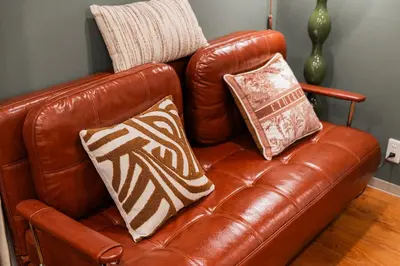 a brown leather couch with two pillows on it at A1 Shibuya , 1 room, 7 mins to ST Max 2P \u6e0b\u8c37\u5168\u65b0\u88c5\u4fee \u4ea4\u901a\u4e2d\u5fc3 \u8f66\u7ad97\u5206\u949f \u6700\u59272\u4eba \u76f4\u8fbe\u65b0\u5bbf \u6d89\u8c37 \u8868\u53c2\u9053 \u54c1\u5ddd \u6c60\u888b \u4e0a\u91ce \u4ee3\u4ee3\u6728 \u94f6\u5ea7 \u539f\u5bbf in Tokyo