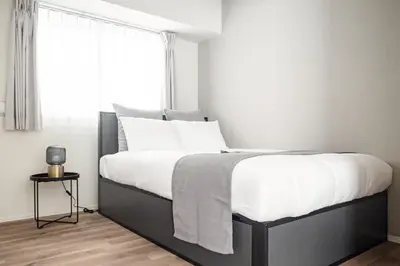a bedroom with a bed with white sheets and a window at ASMACi MAISON\u4e21\u56fd I in Tokyo