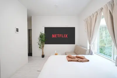 a white bedroom with a bed with a netflix sign on the wall at Vivere in Tokyo