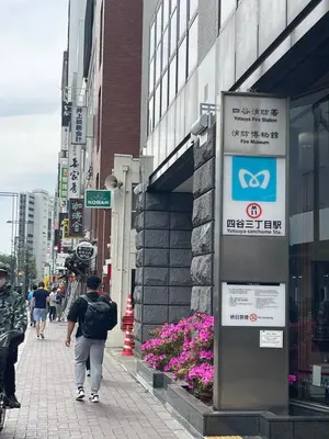 a man walking down a city street with a sign at Yotsuya, 10 seconds from Yotsuya Sanchome Station, in the heart of Shinjuku in Tokyo