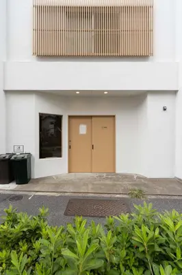 a white building with a brown door and some bushes at \u30a2\u30f3\u30c9\u30b9\u30c6\u30a4\u5f25\u751f\u753a4\u4e01\u76ee201 in Tokyo