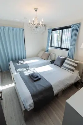 two beds in a bedroom with blue curtains and a chandelier at Tokyo Skytree 101 Elegance Blue Twin w Bath & WC in Tokyo