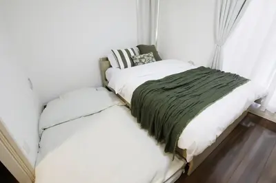a bedroom with a bed with white sheets and green blanket at Guest House KAMEARI 203 in Tokyo