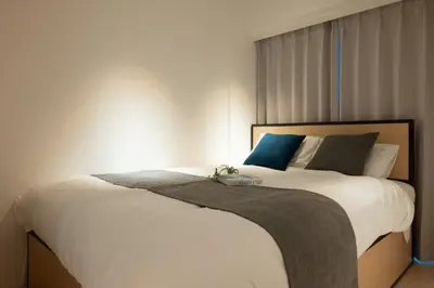 a bedroom with a bed with white sheets and blue pillows at \u30eb\u30cd\u30b5\u30f3\u30b9\u30b3\u30fc\u30c8\u672c\u6240\u543e\u59bb\u6a4b in Tokyo