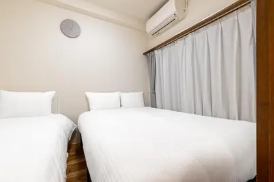 two beds in a room with a clock on the wall at Great location 8 minutes on foot from Higashi-Shinjuku Station and 1 stop from Shinjuku Station! Accommodates up to 11 people Wi-Fi available Shibuya, Asakusa, Ikebukuro in Tokyo