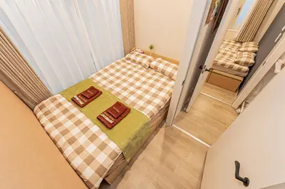 a small bedroom with a bed with a checkered blanket at 80m to Aoto Station Elevator Access 35 Min Direct to Haneda Airport Direct Train to Narita Airport Easy Access to Ginza Asakusa Disney Skytree Convenience Store and Pharmacy Downstairs in Tokyo