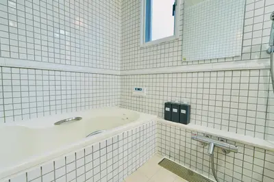 a white tiled bathroom with a tub and a mirror at New Open! Shinjuku 5 bedrooms 3 bathrooms Large Villa 2000 sq ft, kids play room, max 16ppl, 4min train to Shinjuku - Magnolia Hotel Shinjuku in Tokyo