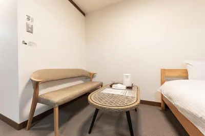 a bedroom with a chair and a bed and a table at Tourist Hotel New Aoki \u89b3\u5149\u30db\u30c6\u30eb \u30cb\u30e5\u30fc\u9752\u6728 in Tokyo