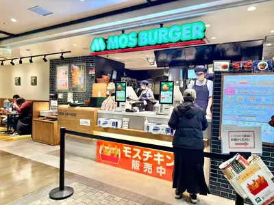 a woman standing in front of a moses burger restaurant at \u30a8\u30de\u30fc\u30ec\u6771\u5c0f\u5ca9205 \u5c0f\u5ca9\u99c5\u5f92\u6b695\u5206 \u6700\u59275\u540d \u548c\u5ba4\u7573 in Tokyo