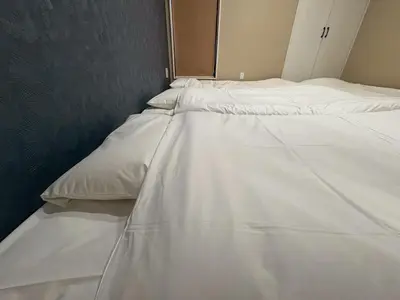 two beds in a room with white sheets at EASE Shinjuku in Tokyo