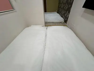two beds in a small room with white sheets at EASE Shinjuku in Tokyo