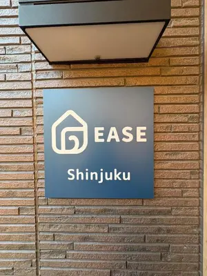 a sign on the side of a brick wall at EASE Shinjuku in Tokyo