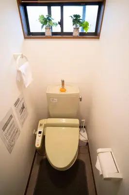 a bathroom with a toilet with a window and two plants at Kimiko Jujo House - Local Art Stay 11 min Shinjuku in Tokyo