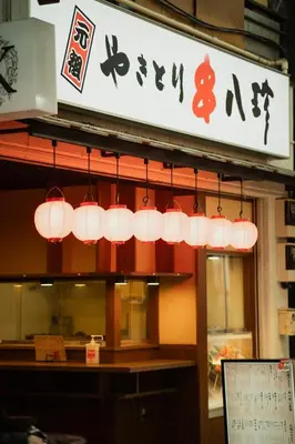 a row of lights hanging from the front of a restaurant at Kimiko Jujo House - Local Art Stay 11 min Shinjuku in Tokyo