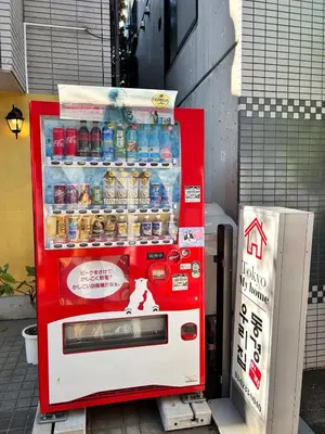 a red soda machine sitting on the street at 3 min from Shin-Okubo l Private Single Room in Tokyo