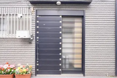 a gray garage with a door and two potted flowers at R-Styles \u6e0b\u8c37 in Tokyo