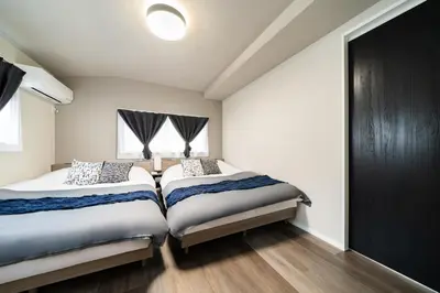 two beds in a bedroom with white walls and wood floors at 109, Nishiarai, \u897f\u65b0\u4e95 \u65b0\u898f\u30aa\u30fc\u30d7\u30f3, \u6771\u4eac\u89b3\u5149\u306b\u6700\u9069, 10\u540d\u69d8\u3054\u5229\u7528\u53ef\u80fd in Tokyo