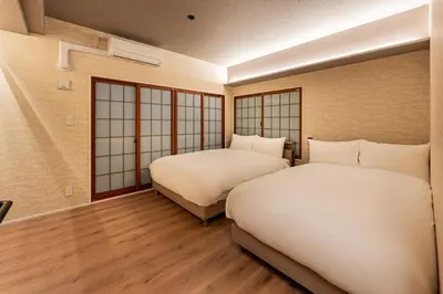 two beds in a room with wooden floors and windows at Cocono Apartment Hotel in Tokyo