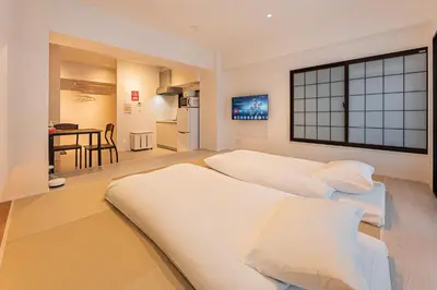 a bedroom with two white beds and a kitchen at Cocono Apartment Hotel in Tokyo