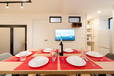 a dining room table with white plates and a bottle of wine at Yuka House Komagome 1\u968e \u81ea\u8ee2\u8eca\u4ed8 \u304a\u3082\u3061\u3083\u3068\u843d\u66f8\u304d\u58c1\u306e\u30d7\u30ec\u30a4\u30eb\u30fc\u30e0 \u5bb6\u65cf\u5411\u3051 in Tokyo