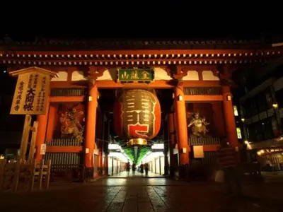 a building with a giant face hanging from it at night at Shitamachi Base in Tokyo