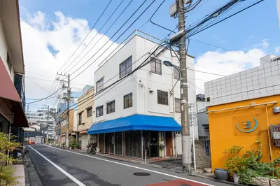 a city street with a white building with a blue awning at HanaStay-Tokyo Ueno 2 Stops in Tokyo