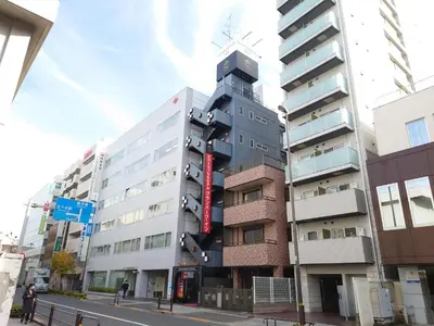 a tall building with a red sign on the side of it at Spa&Capsule Hotel Grandpark Inn Kitasenju in Tokyo