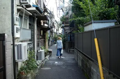 a woman walking down a narrow alley with buildings at hanare in Tokyo