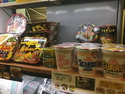 a store shelf filled with lots of cups of food at Capsule Land Yushima (Male Only) in Tokyo