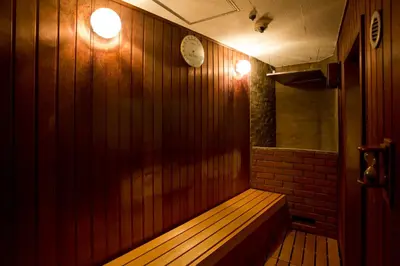 a wooden bench in a room with a clock on the wall at Capsule Land Yushima (Male Only) in Tokyo