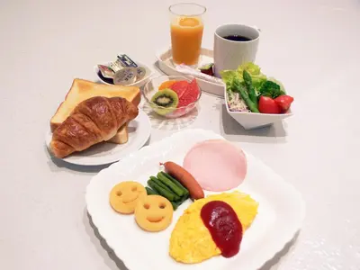 a table with plates of breakfast foods and a glass of juice at Shinjuku City Hotel N.U.T.S Tokyo in Tokyo