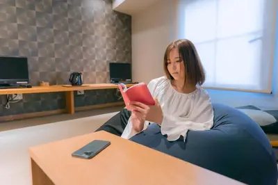 a woman sitting in a chair reading a book at NADESHIKO HOTEL TOKYO Shibuya by unito Female-only in Tokyo