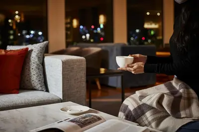 a woman holding a cup of coffee in a living room at Keio Plaza Hotel Tokyo in Tokyo