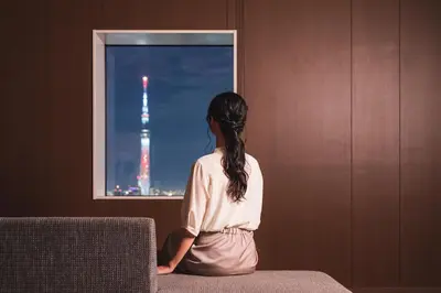 a woman sitting on a chair looking out a window at the eiffel tower at Hotel Crown Hills Ueno Premier in Tokyo