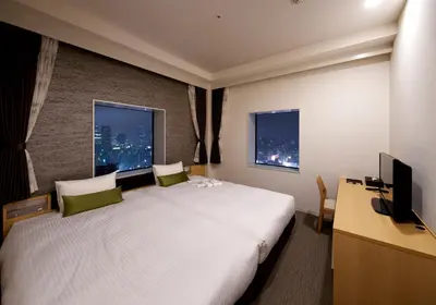 a hotel room with a bed and a desk and two windows at Hotel Crown Hills Ueno Premier in Tokyo