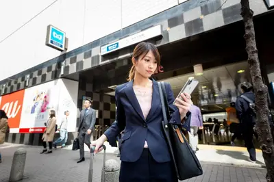 a woman holding a cell phone in front of a building at Akasaka-no Sato (Female Only) in Tokyo