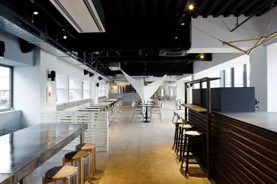 a row of tables and stools in a room with white walls at LYURO Tokyo Kiyosumi by THE SHARE HOTELS in Tokyo