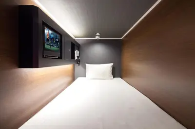 a small room with a bed with a tv on the wall at commun SHIBUYA (Male Only) in Tokyo