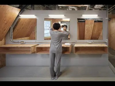 a woman standing in front of a bathroom mirror at Do-C Gotanda in Tokyo